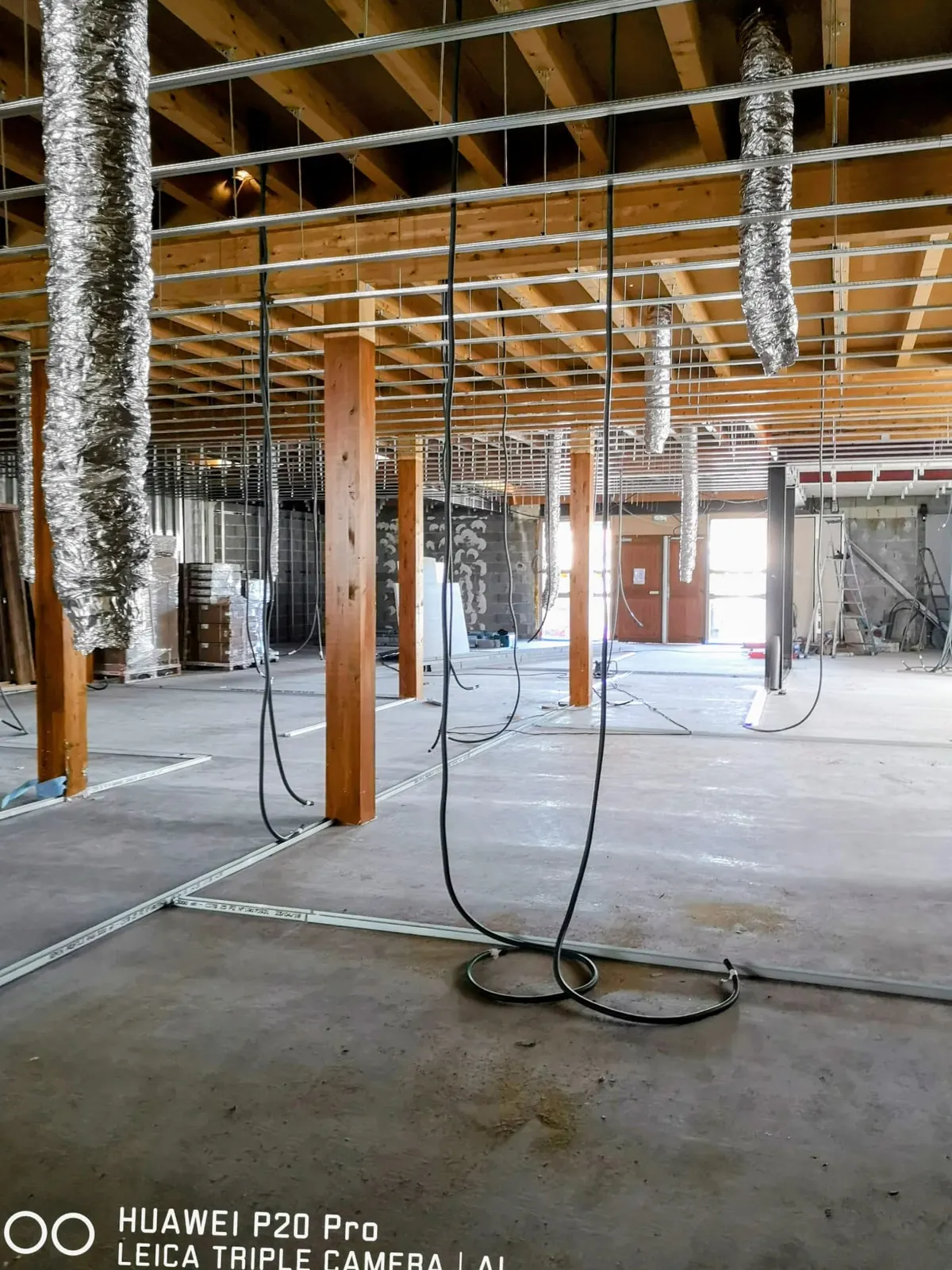 Plateau commercial en rénovation avec charpente bois, gaines de ventilation suspendues et rails de cloisons posés au sol