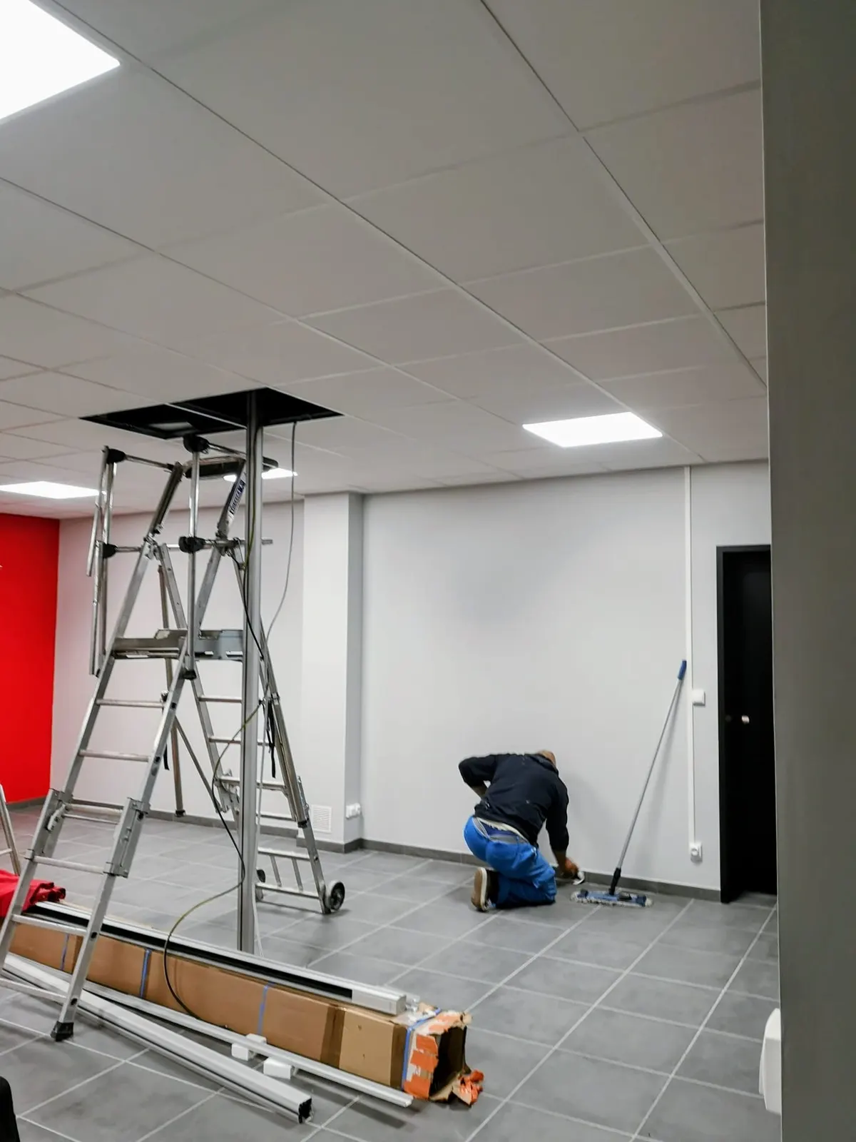 Rénovation d'un local professionnel : faux plafond en dalles blanches, dalles LED et peinture des murs avec mur d'accent rouge
