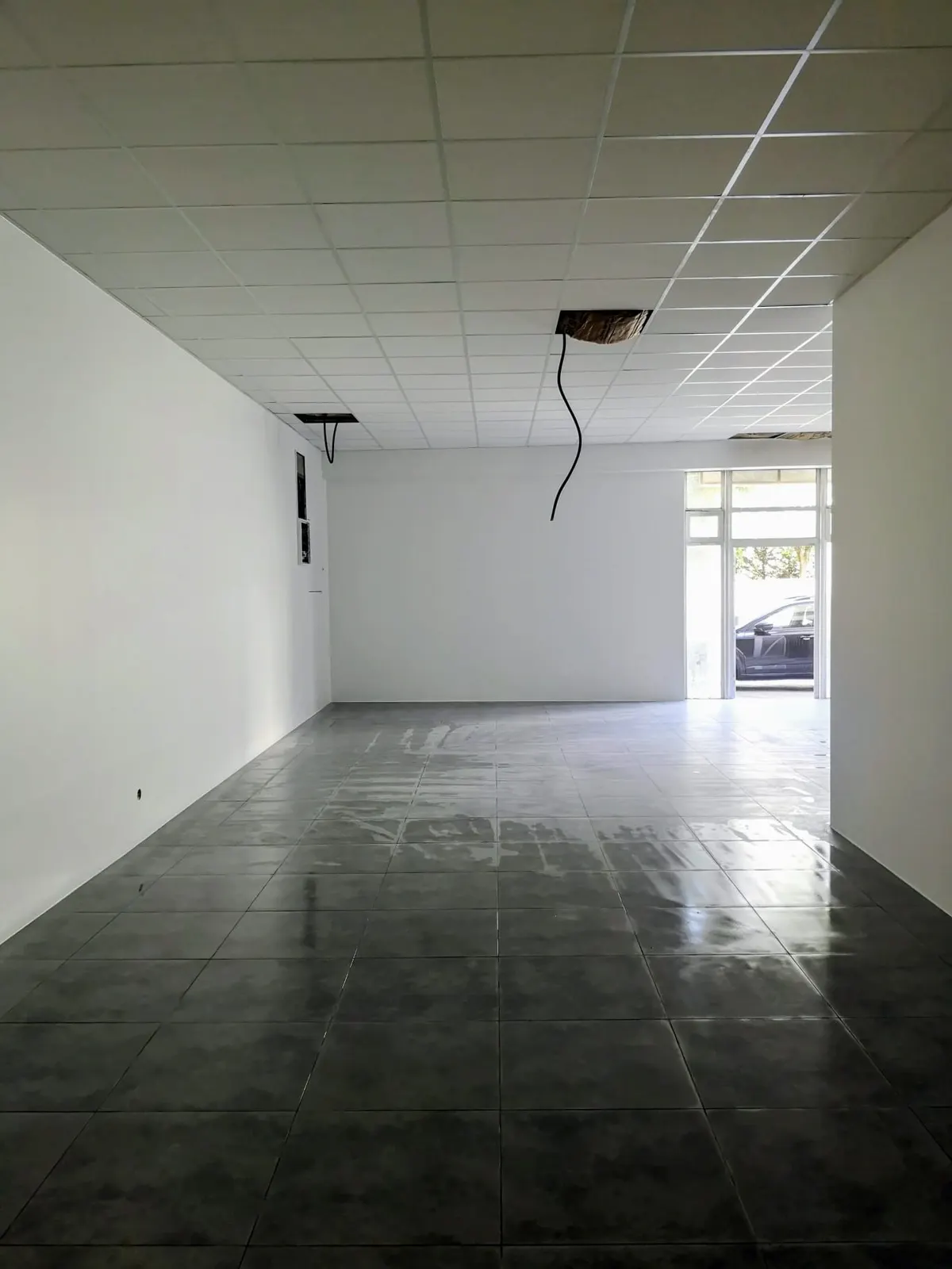 Local commercial vide aux murs blancs repeints, plafond suspendu et carrelage gris en rénovation