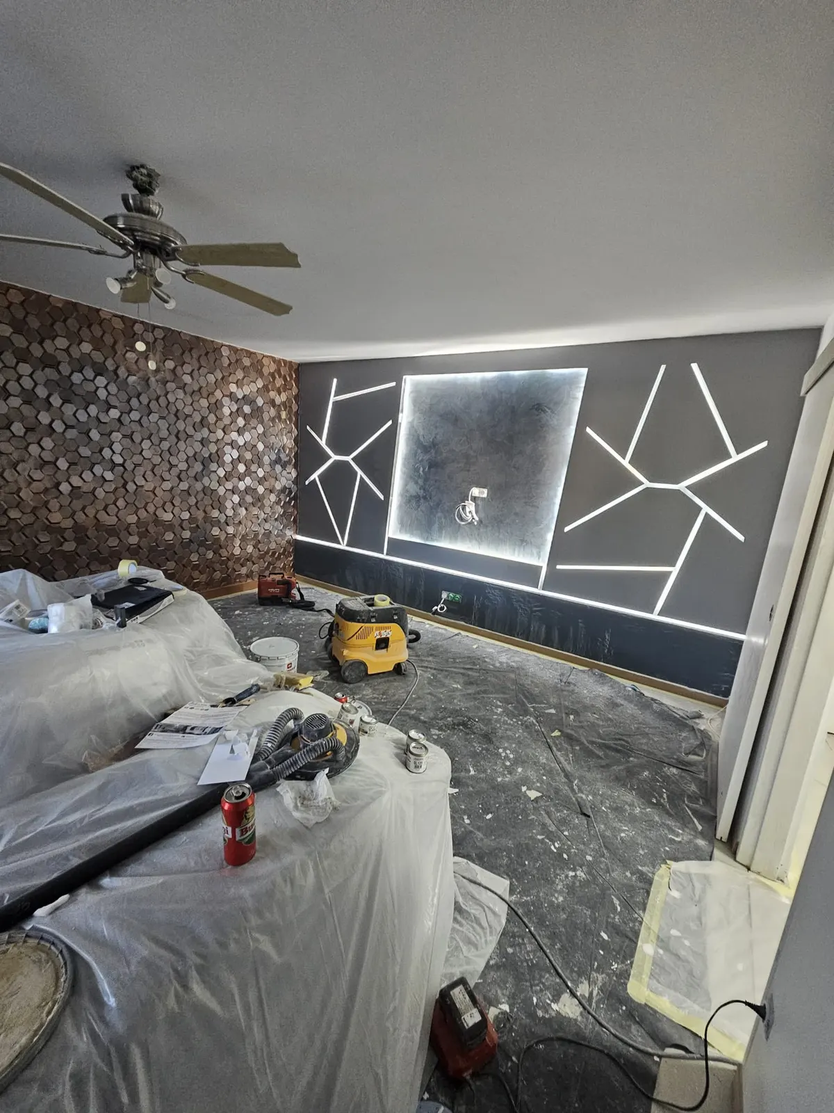 Salon en chantier, mur décoratif anthracite avec LED, mobilier bâché et aspirateur de chantier