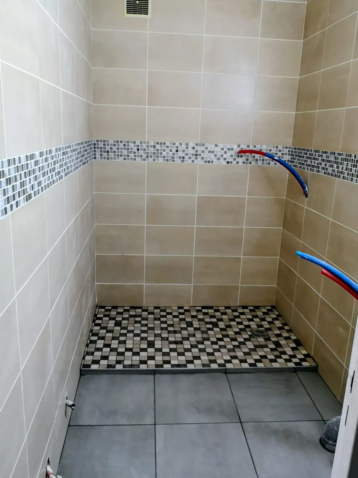 Douche à l'italienne carrelée avec faïence beige et frise mosaïque, arrivées d'eau en attente