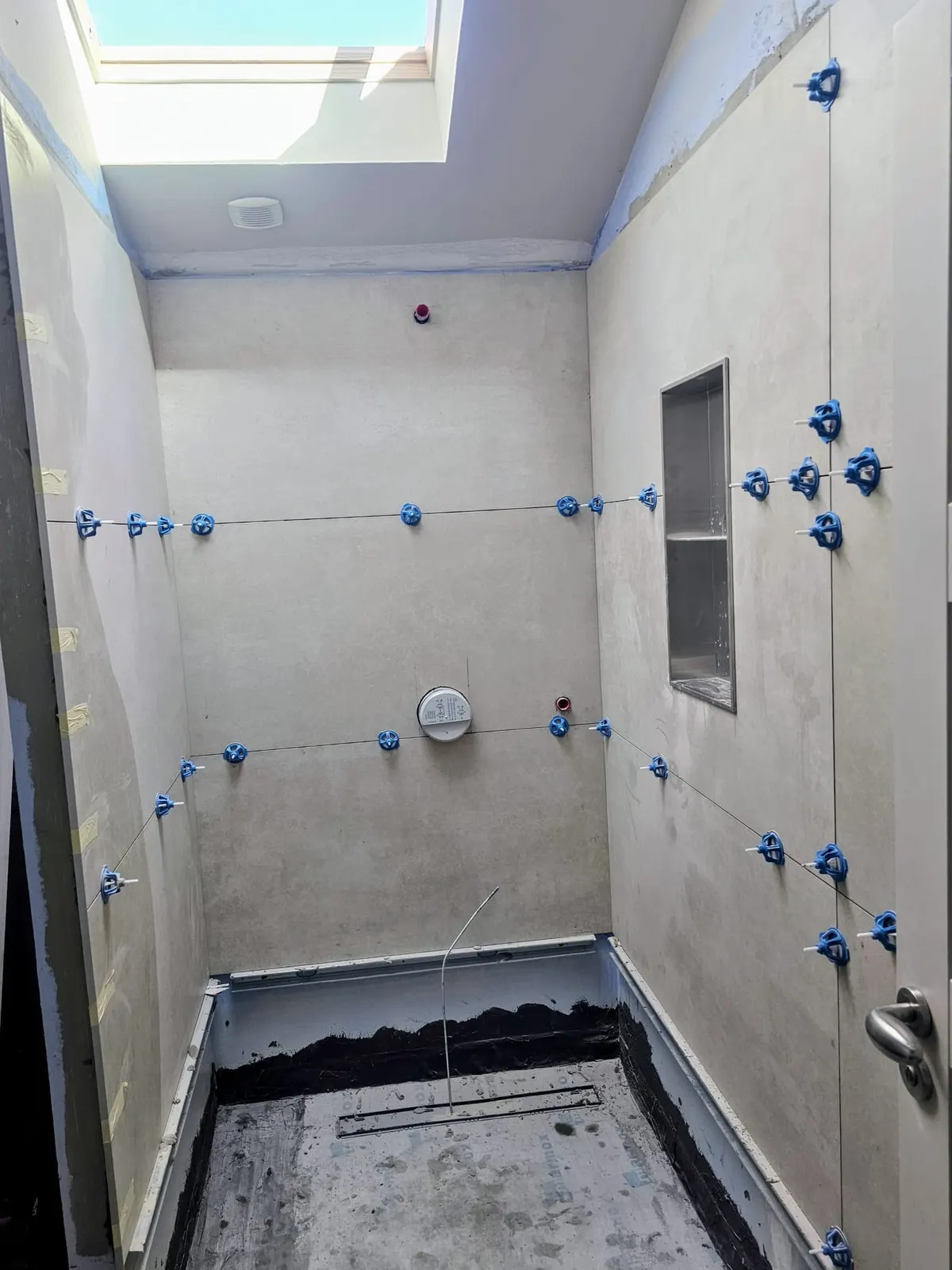 Pose de faïence dans une douche à l'italienne avec niche murale, croisillons bleus et fenêtre de toit