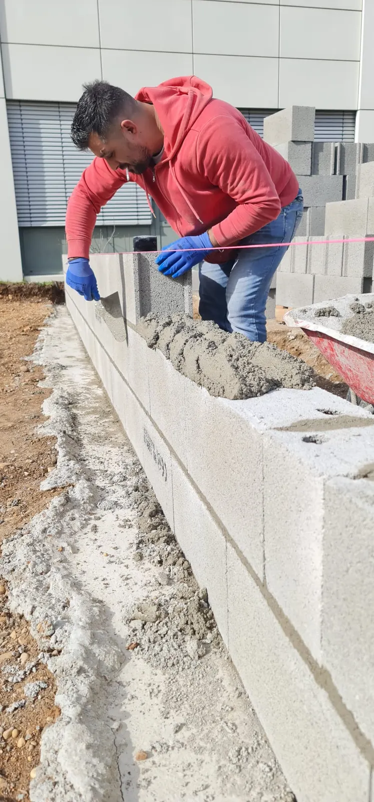 Maçon montant un mur en parpaings au cordeau, chantier extérieur avec mortier frais