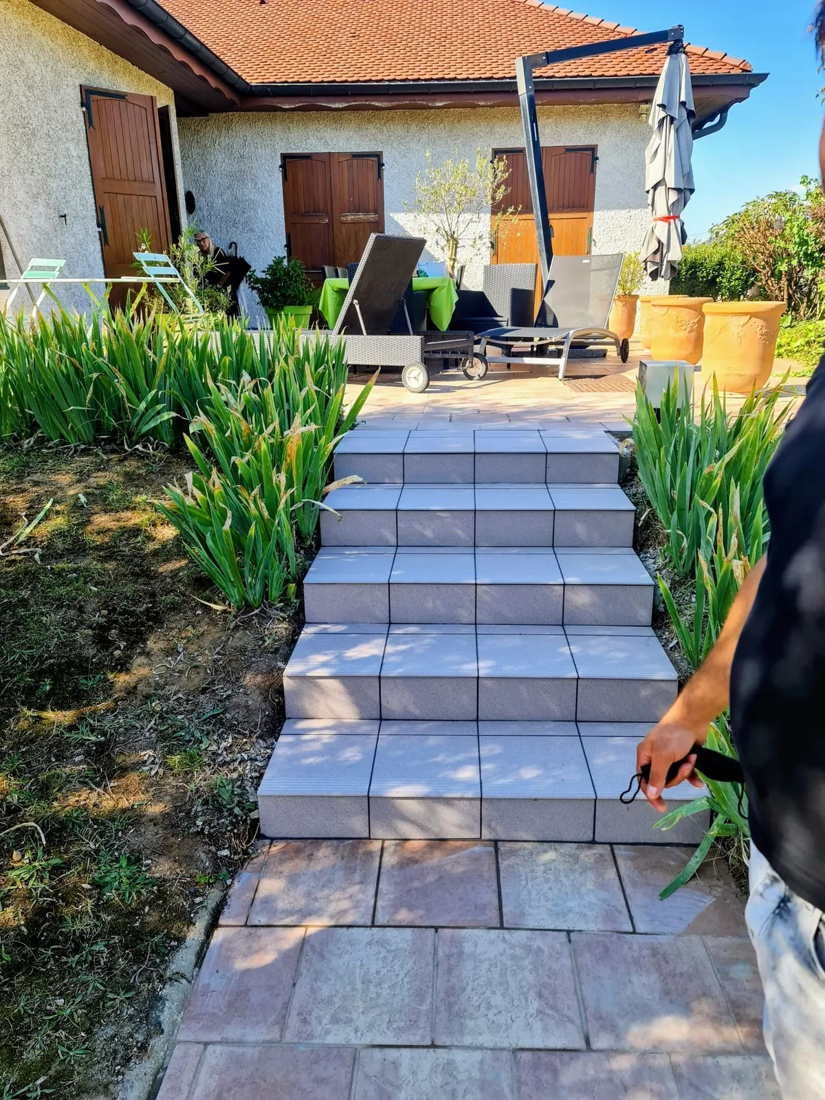 Escalier extérieur en dalles béton gris menant à une terrasse de jardin devant une maison