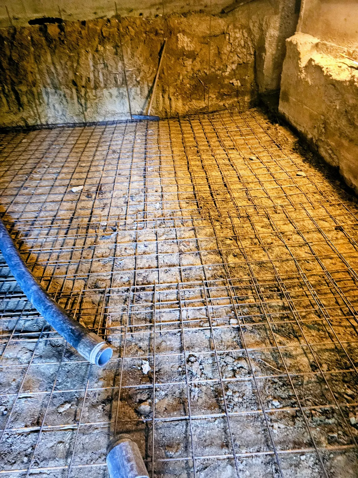 Préparation d'une dalle béton : treillis soudé ferraillé posé avant coulage, avec fourreau bleu et parois en parpaings