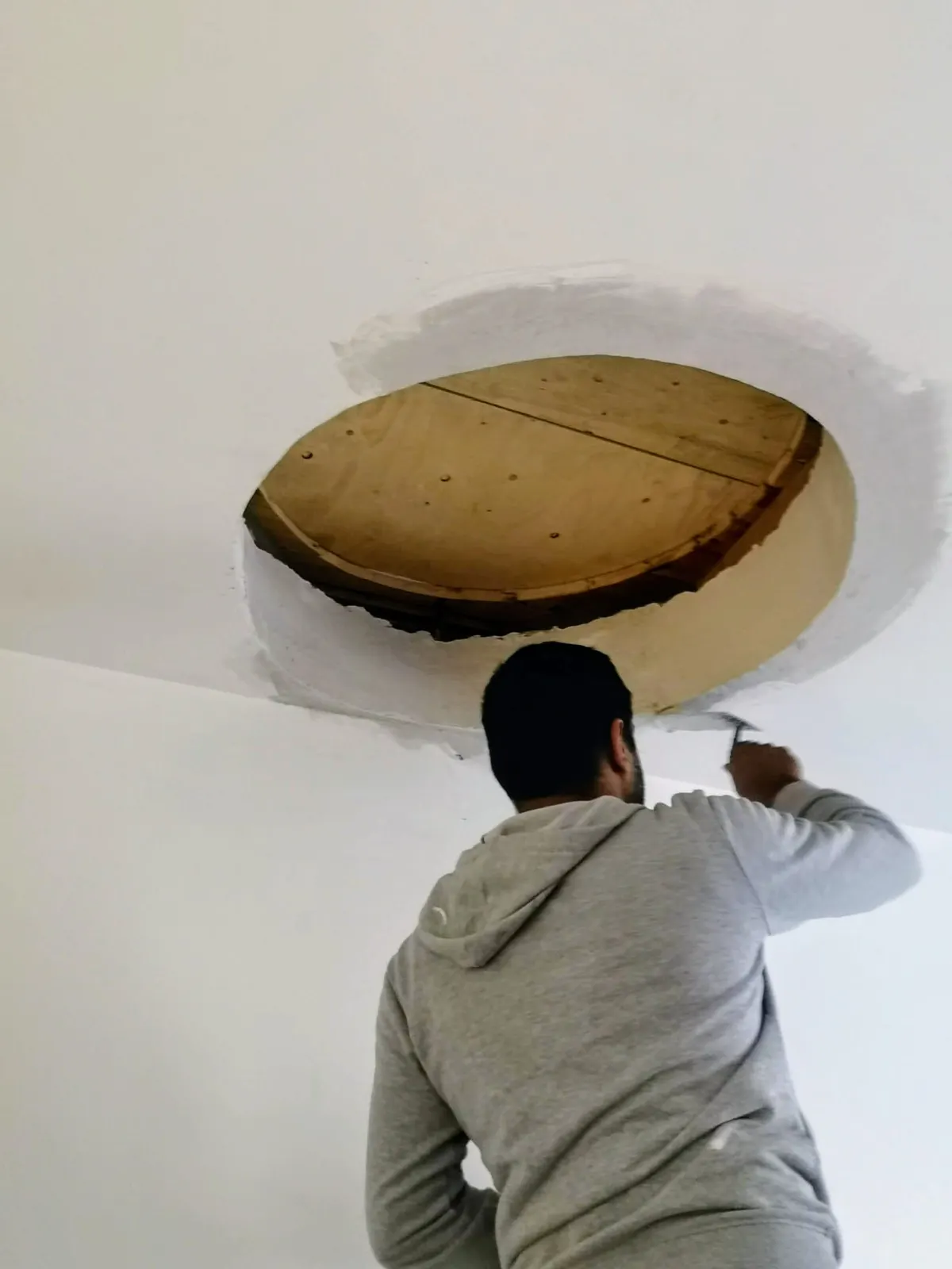Artisan réalisant les finitions plâtre autour d'une ouverture ronde au plafond