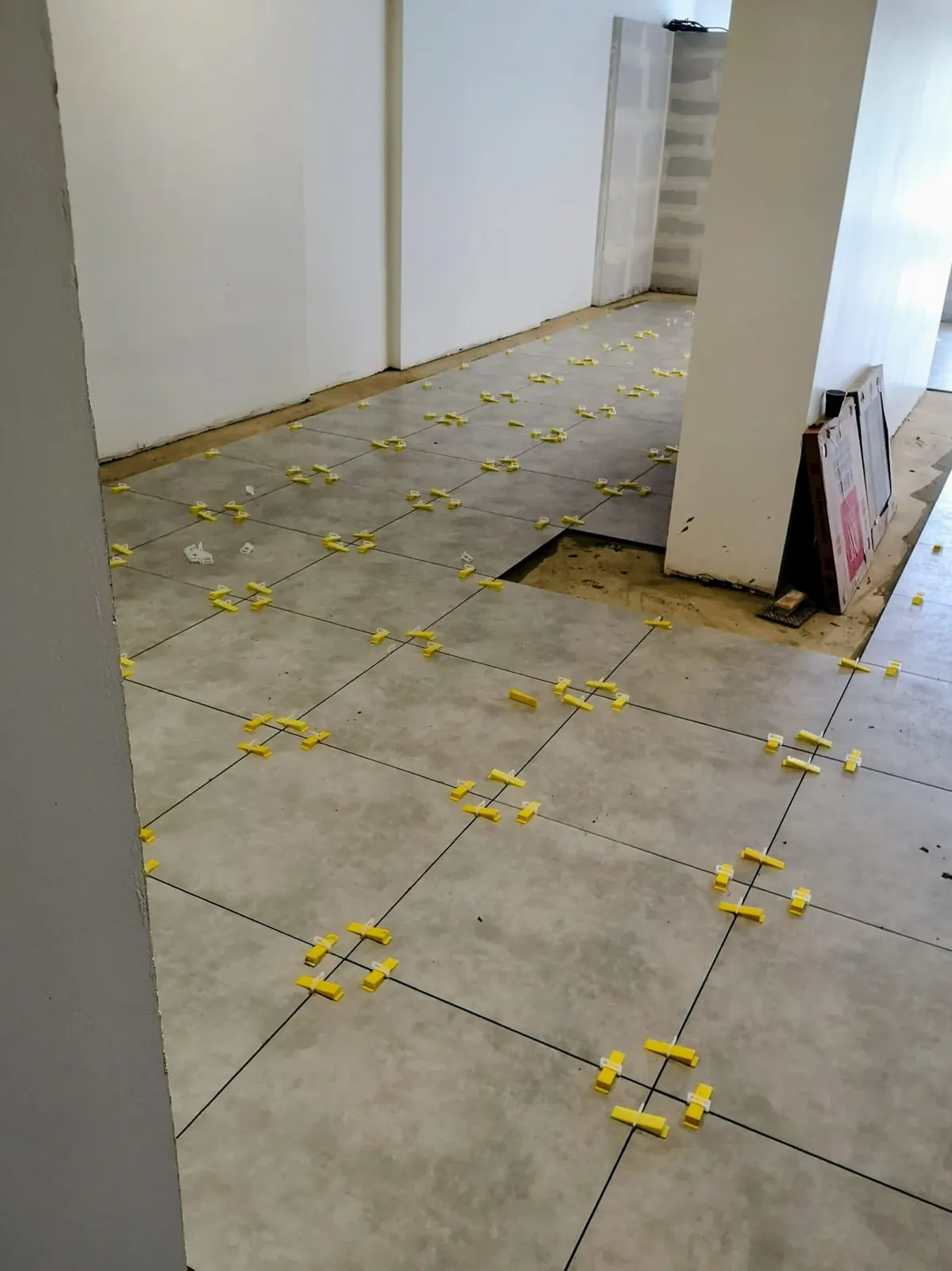 Pose de carrelage gris effet béton au sol avec croisillons et clips de nivellement jaunes