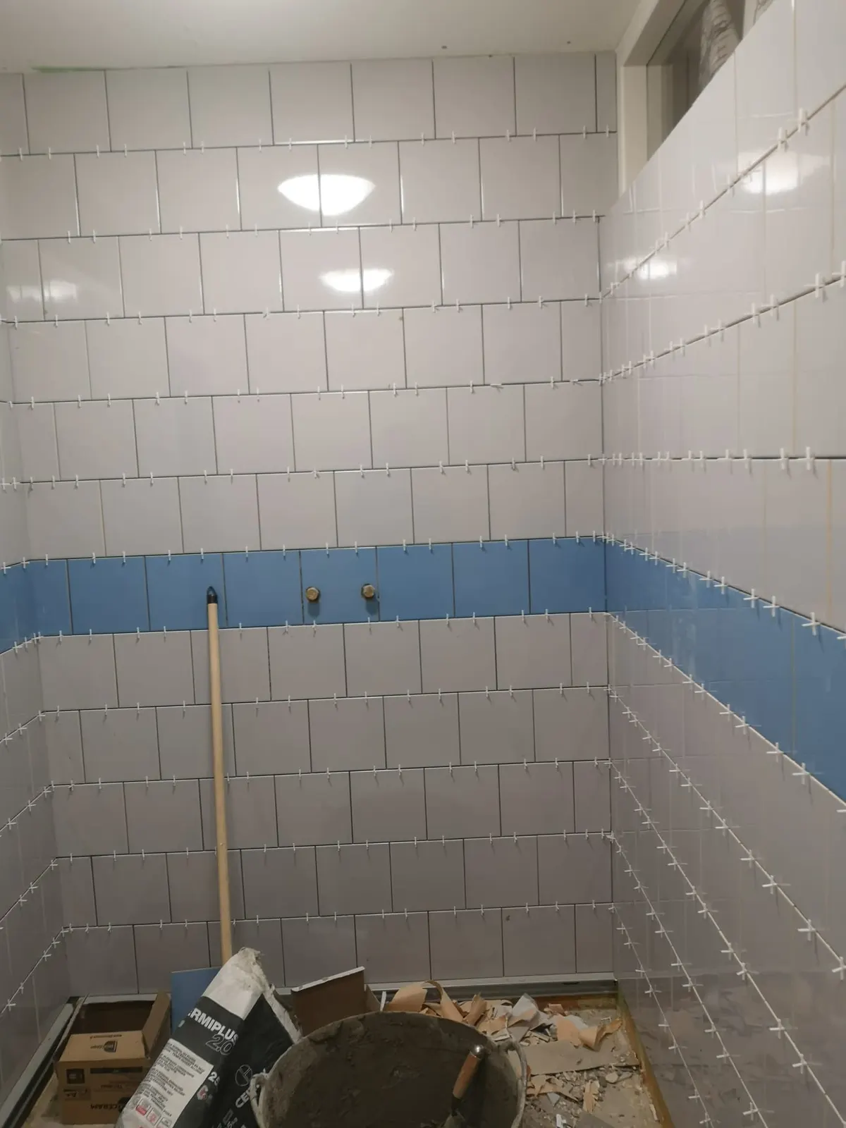 Pose de faïence murale blanche, bleue et grise dans une salle de bain